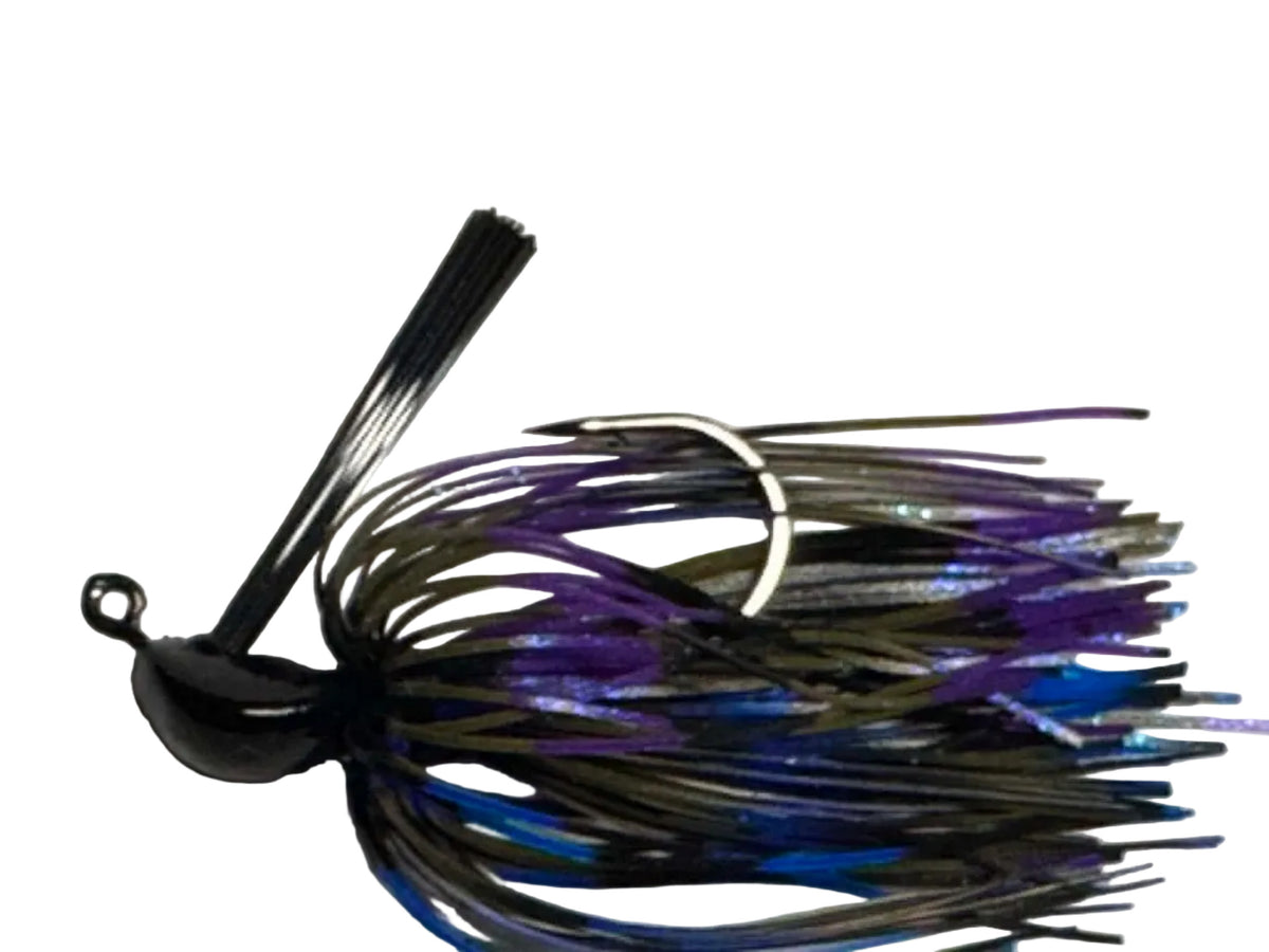 A close-up of a fishing jig lure with a black top, dark metallic skirt, and purple and blue glitter strands, photographed against a plain off-white background.